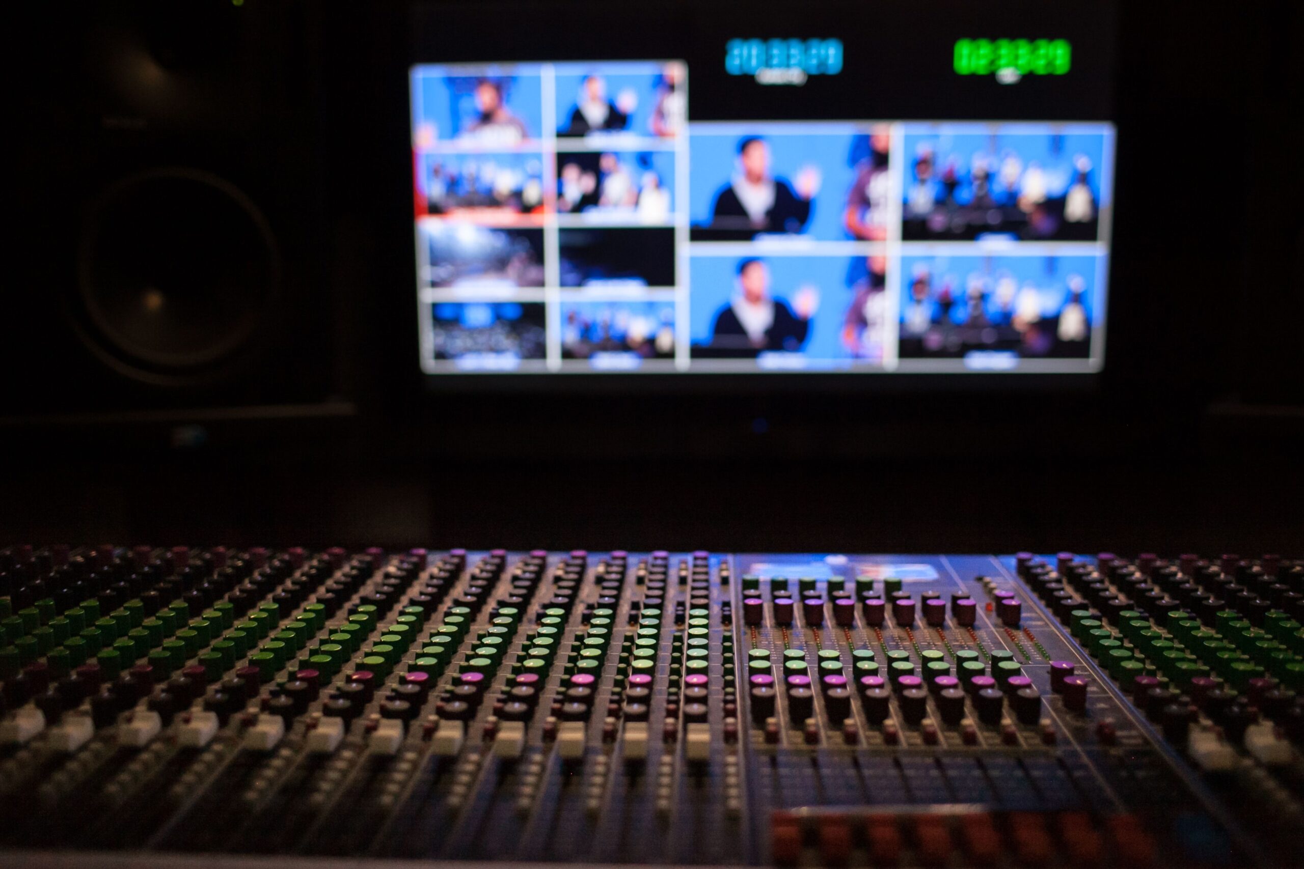 SATA Recordings Close-up of a sound mixer with screens displaying video feeds in a professional studio setup.